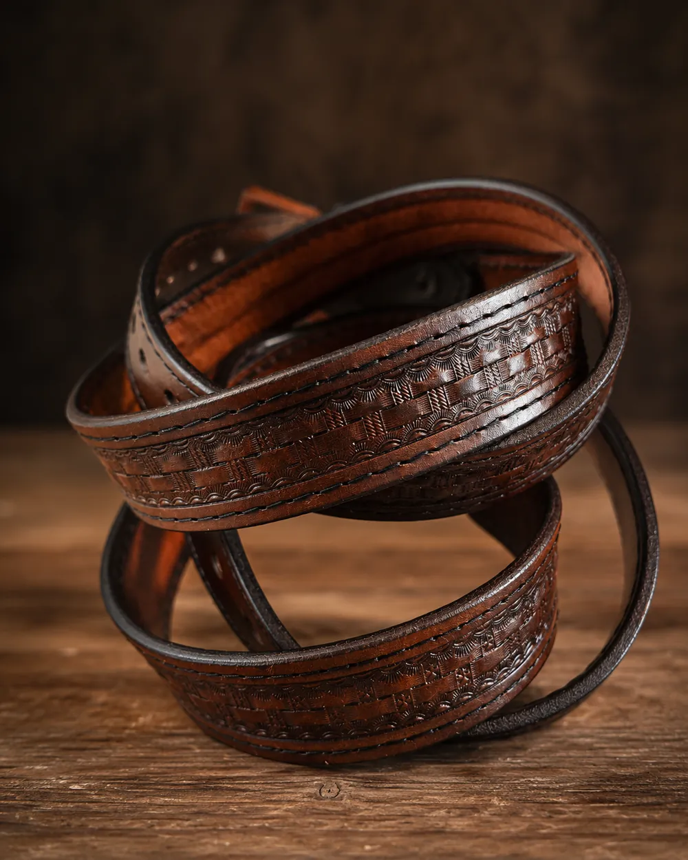 Dark brown leather belt hand-tooled in a basketweave pattern, coiled on weathered wood